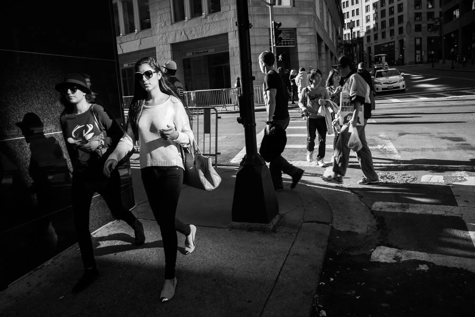 Two women in sunglasses step off a crowded crosswalk into shadow