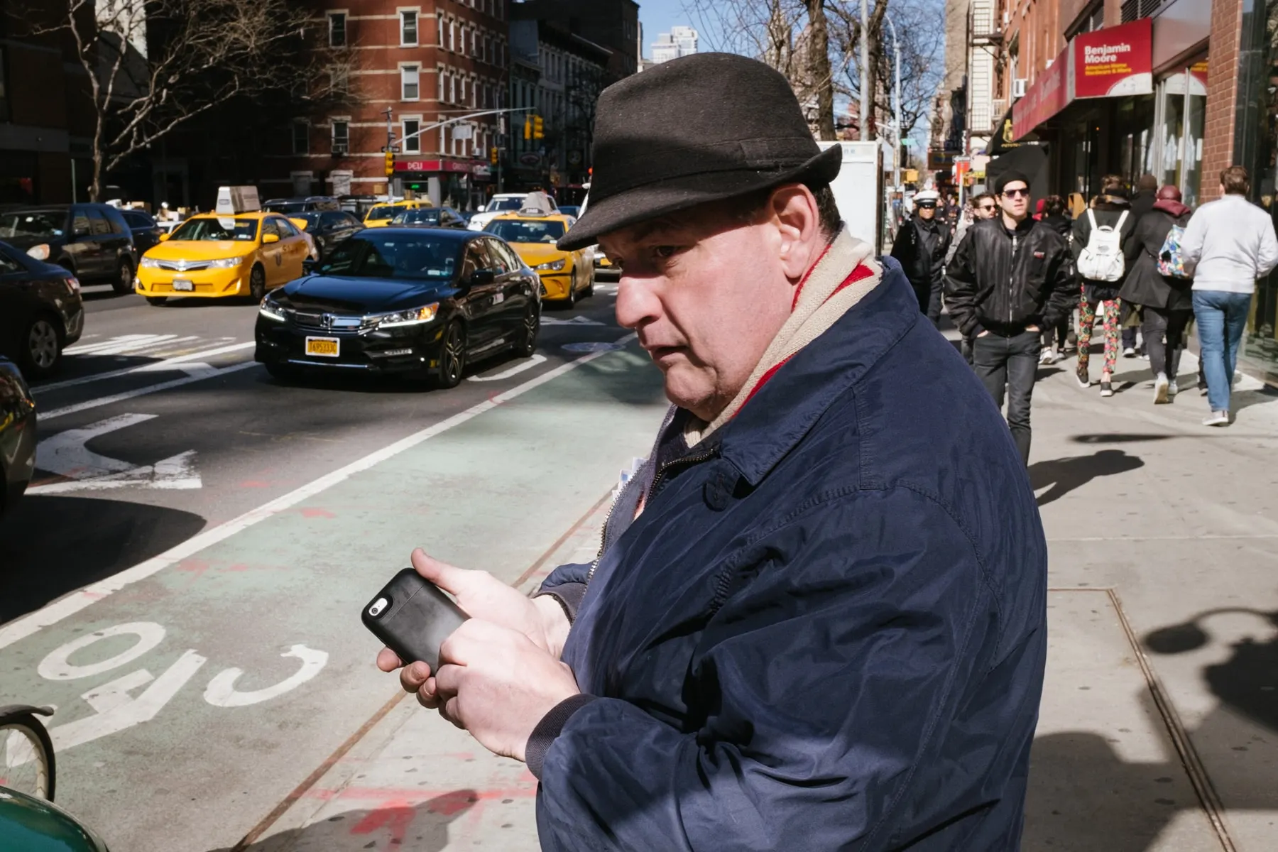 Man in a hat checks his phone at the edge of a street full of yellow cabs