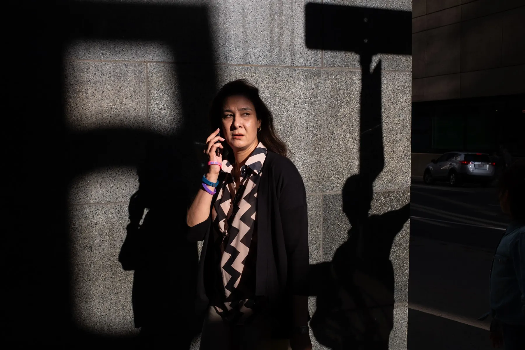 Woman on the phone stands in a patch of light against a stone wall