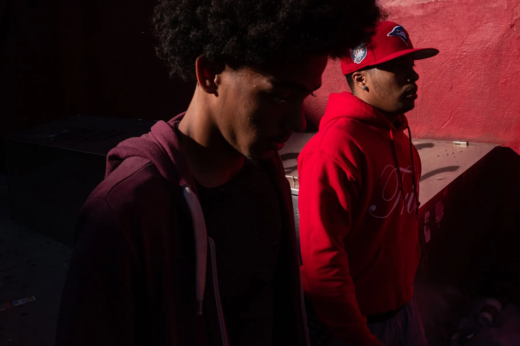 Two young men in red pass a bright pink wall in low light