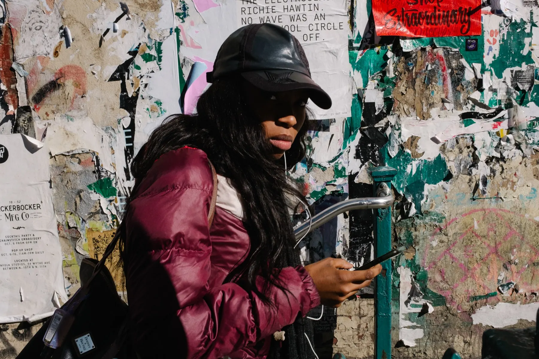 Woman in a magenta puffer jacket passes a wall thick with torn posters