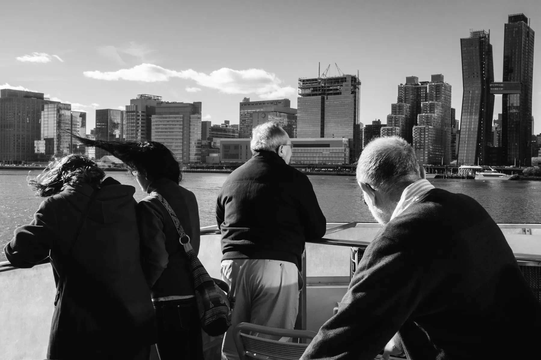 Ferry passengers lean on the rail watching the Manhattan skyline