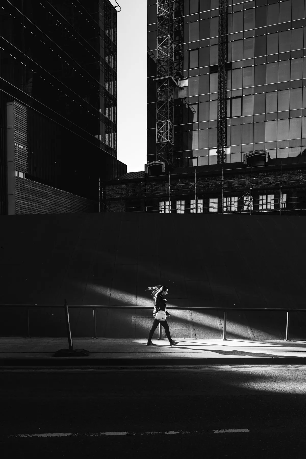 Lone figure crosses a narrow band of light at the foot of a dark glass tower