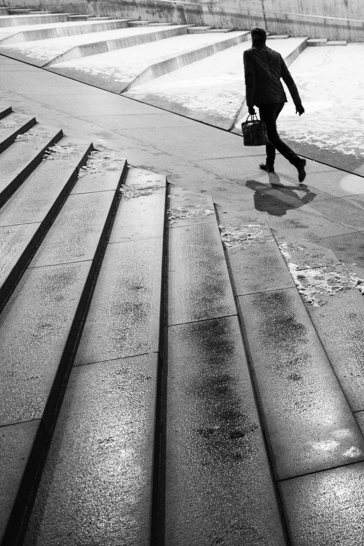 Man with a briefcase crosses wet granite steps, his shadow stretched beside him