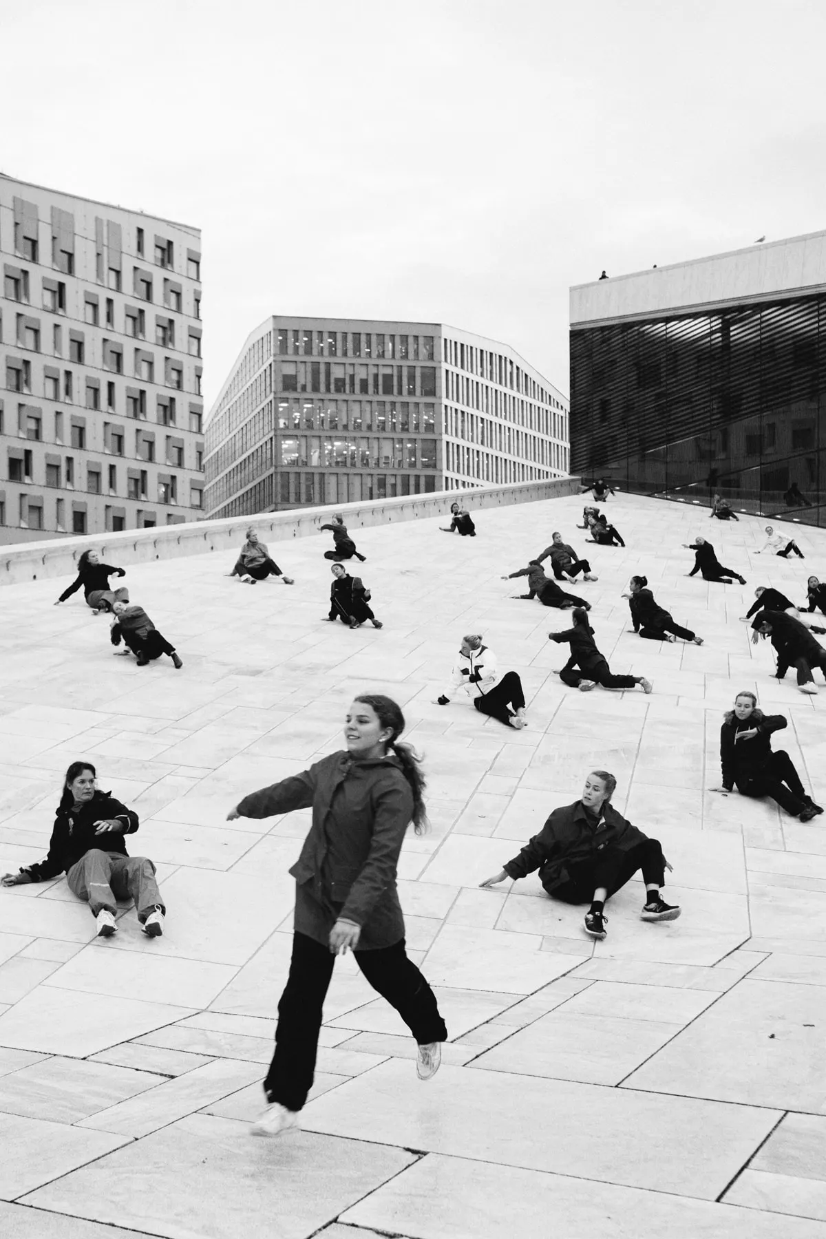 Girl runs across a paved plaza scattered with people sitting on the ground