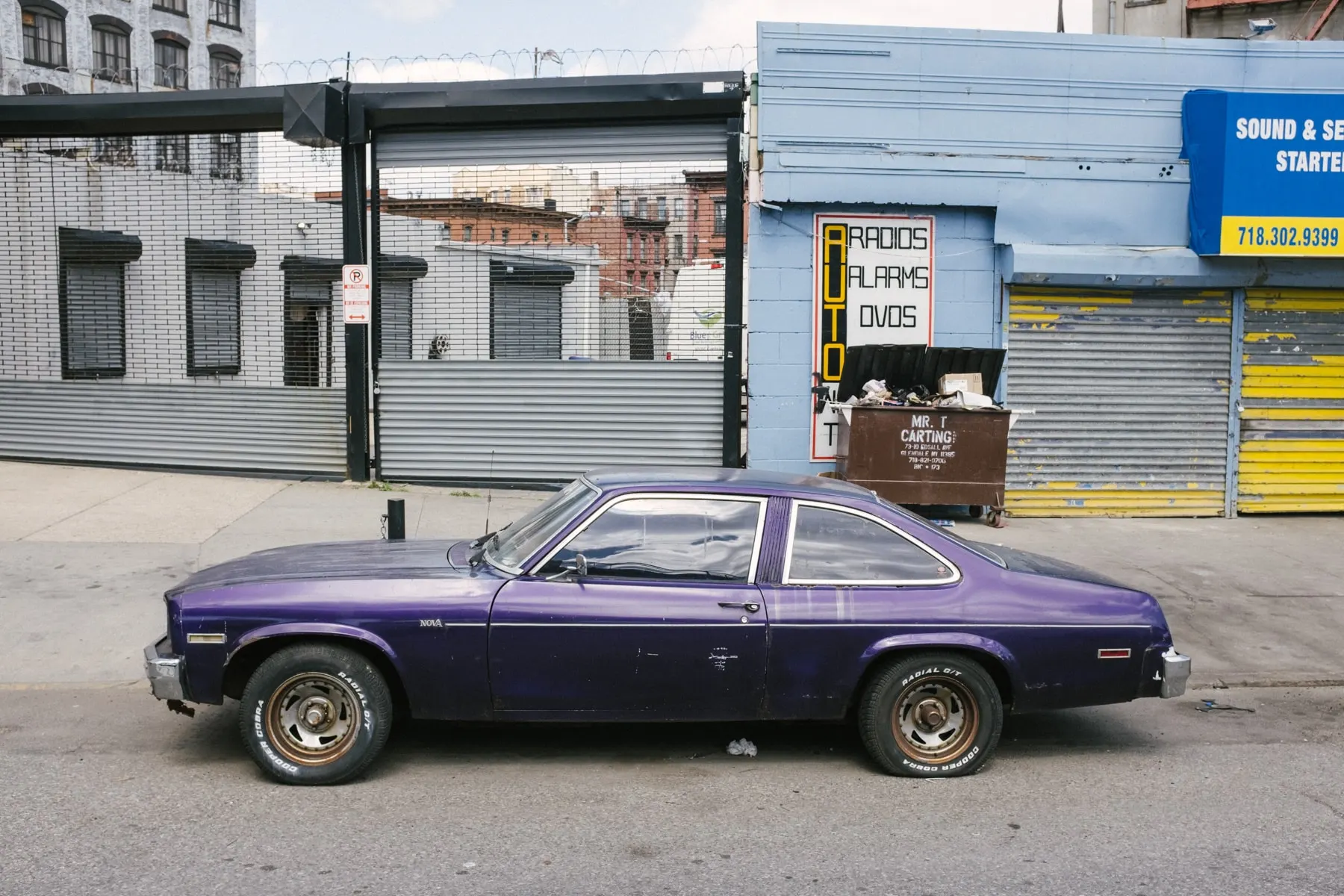 Purple coupe parked outside a shuttered car audio shop