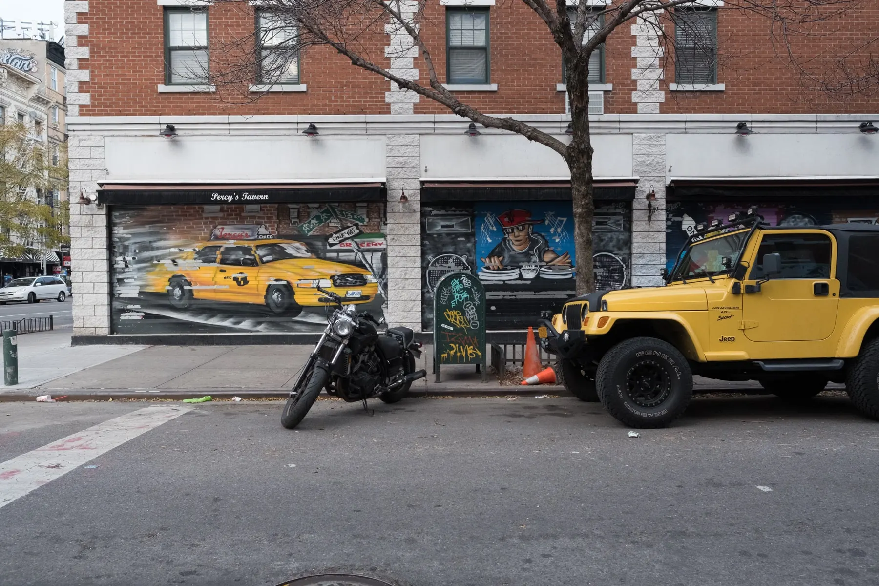 Yellow Jeep and a motorcycle outside a mural of yellow cabs