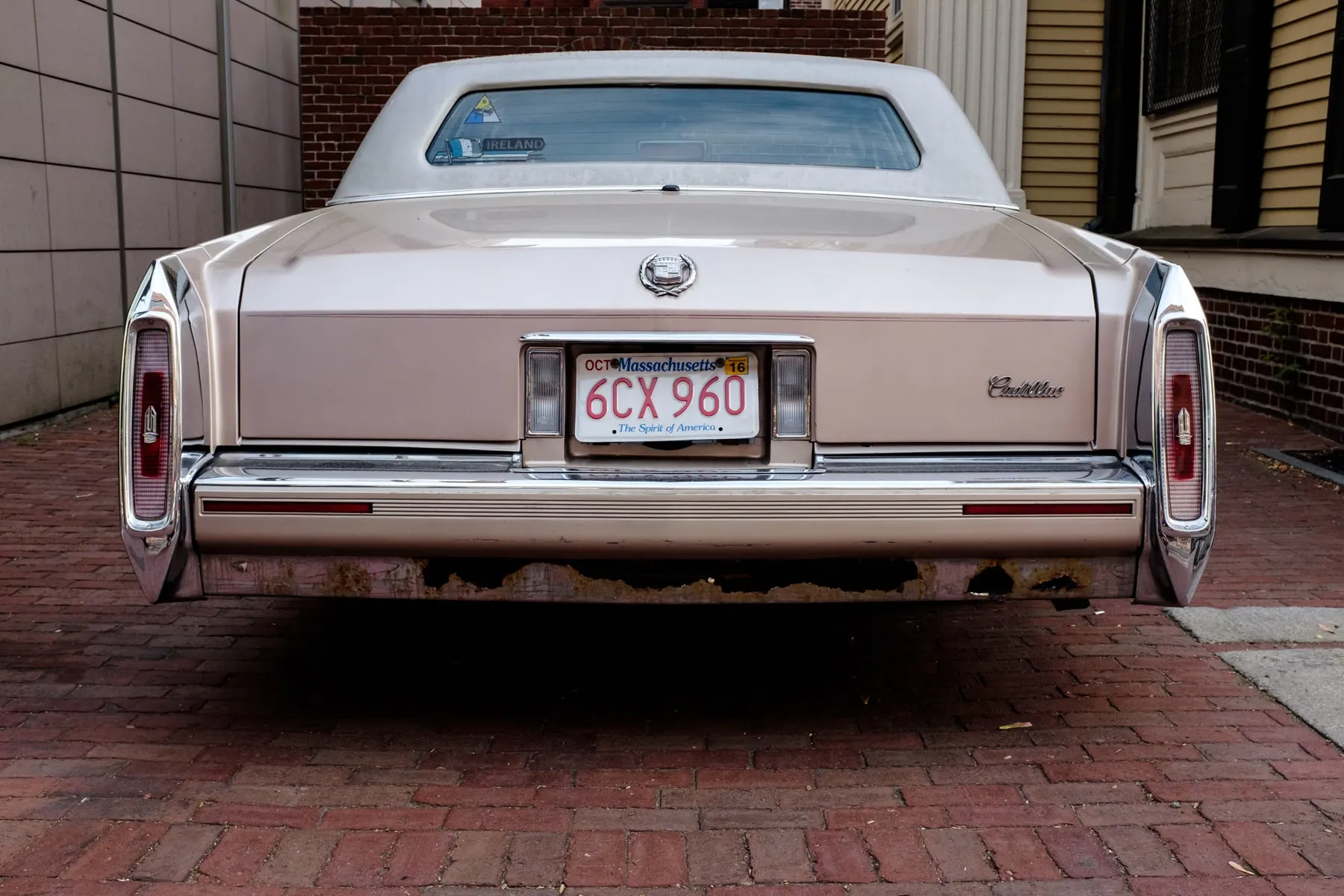 Rear of a pale Cadillac parked on a brick pavement