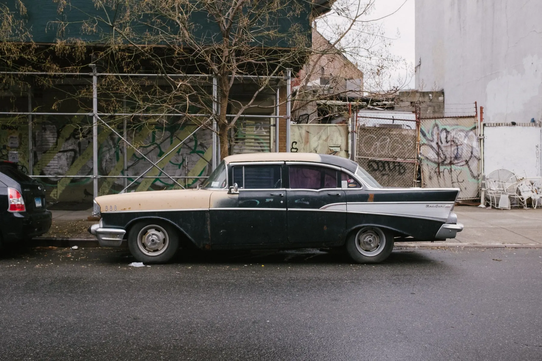 Black and cream fifties sedan parked by a graffitied lot
