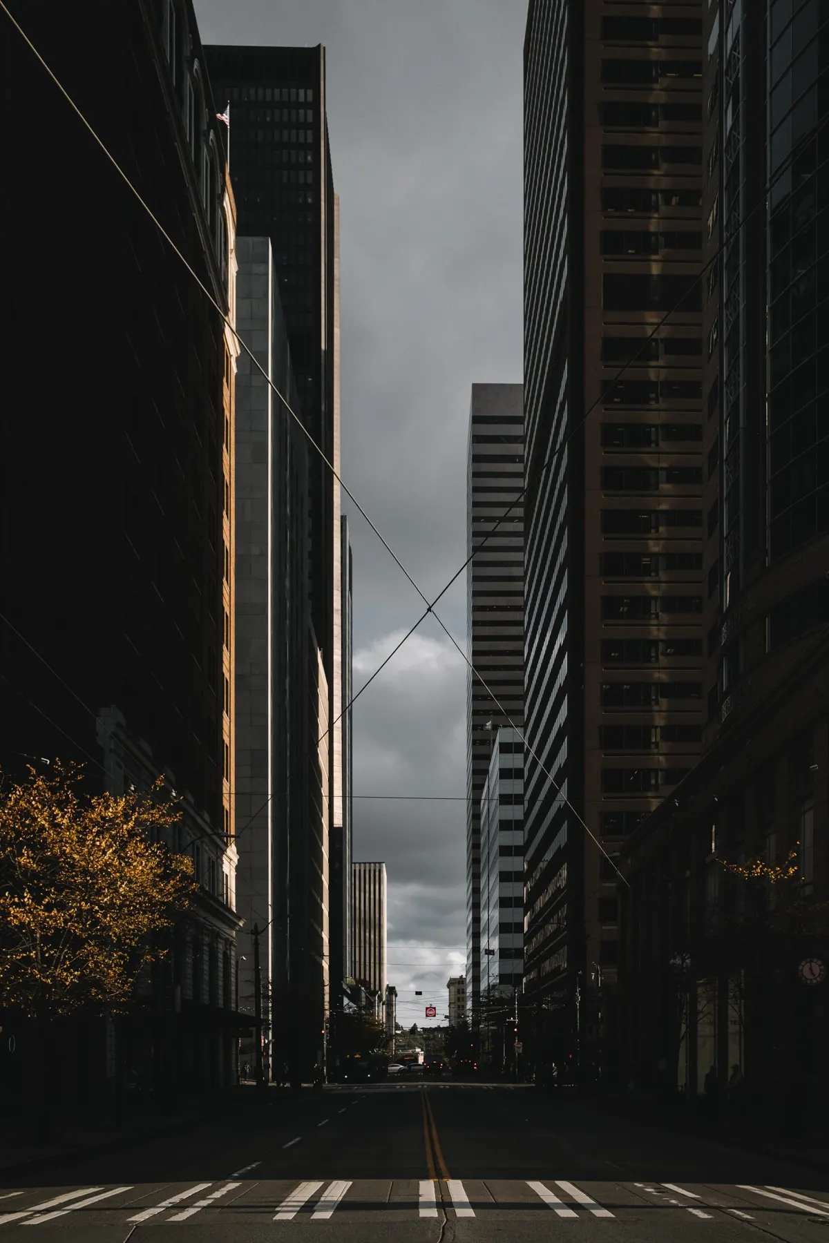 Wires crossing a narrow street between dark towers under a grey sky
