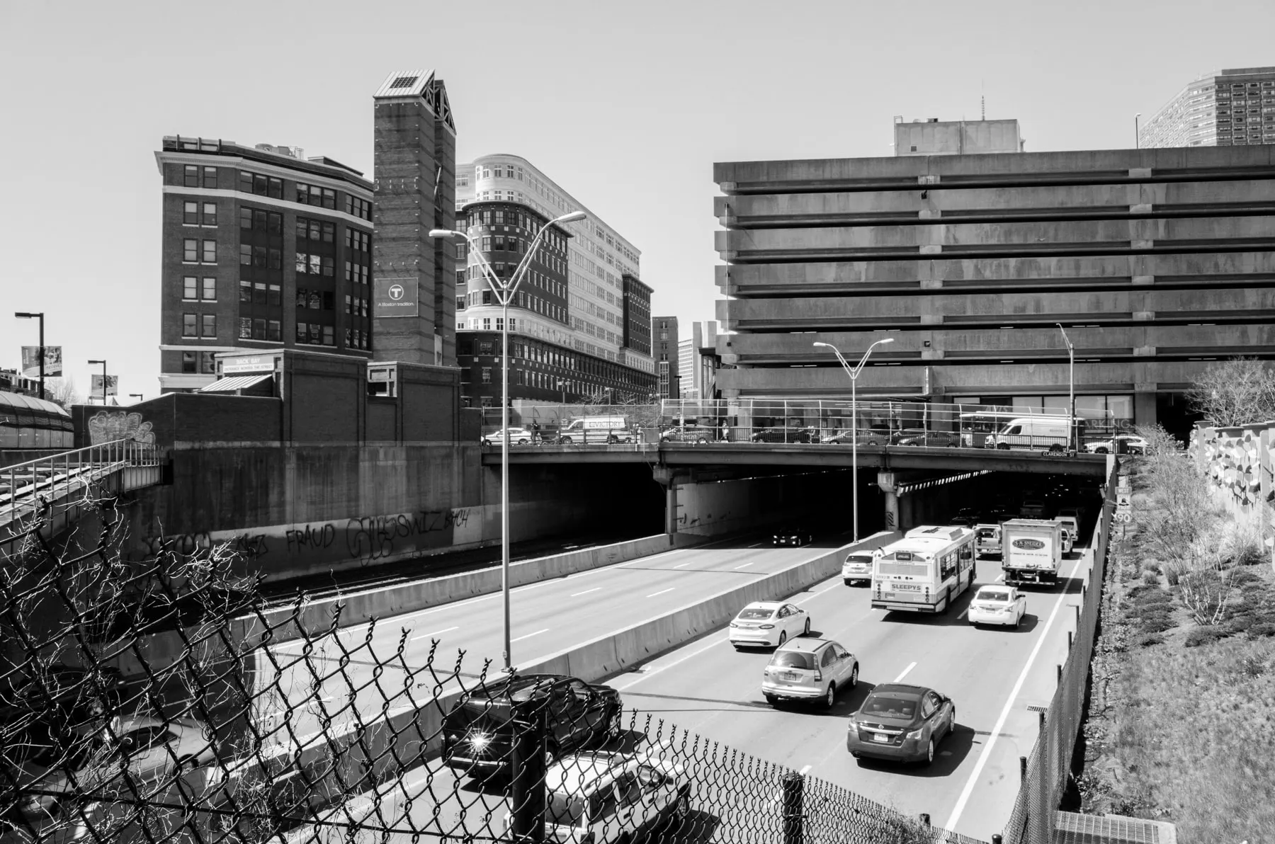 Cars on a sunken highway seen through a chain-link fence