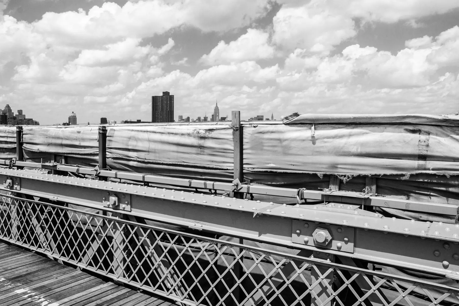 Bridge girders and a wooden walkway, city skyline beyond