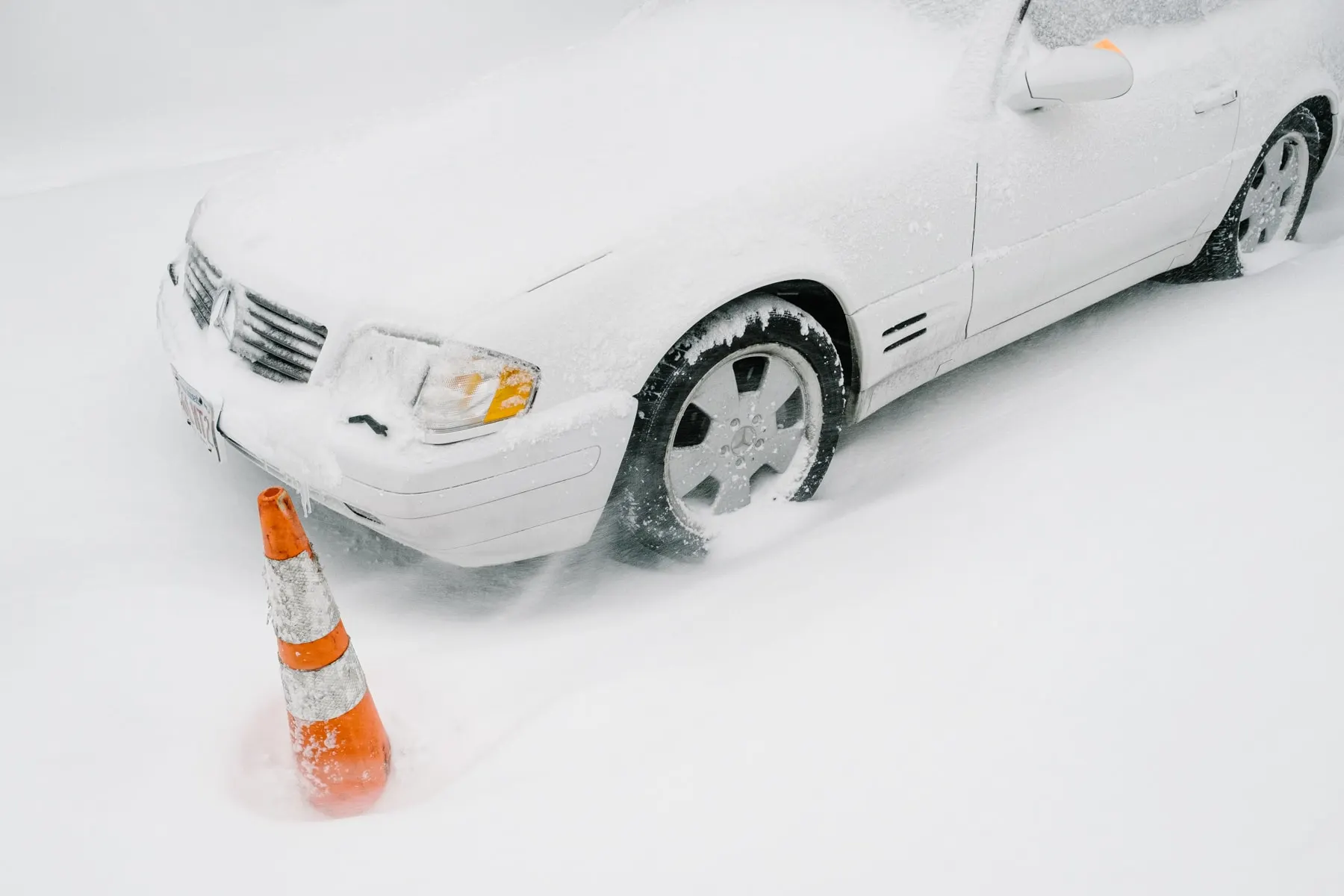 Cone half buried in snow beside a snow-covered car